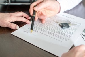 Man handing a pen to a woman to sign a contract, with vehicle keys on the paper