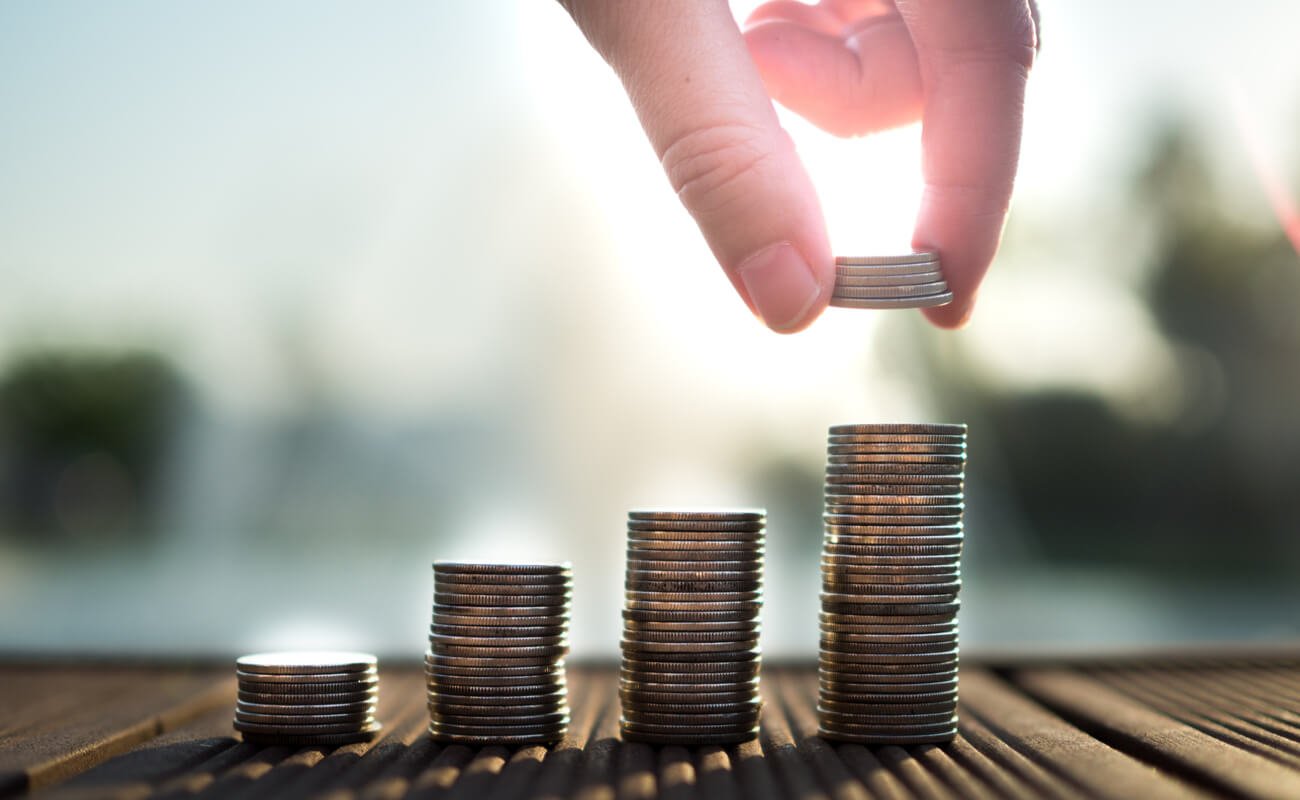 Coins being stacked in ascending columns, with a hand placing more coins on the highest one
