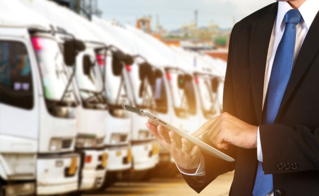 Man in a suit managing a fleet of trucks with a tablet