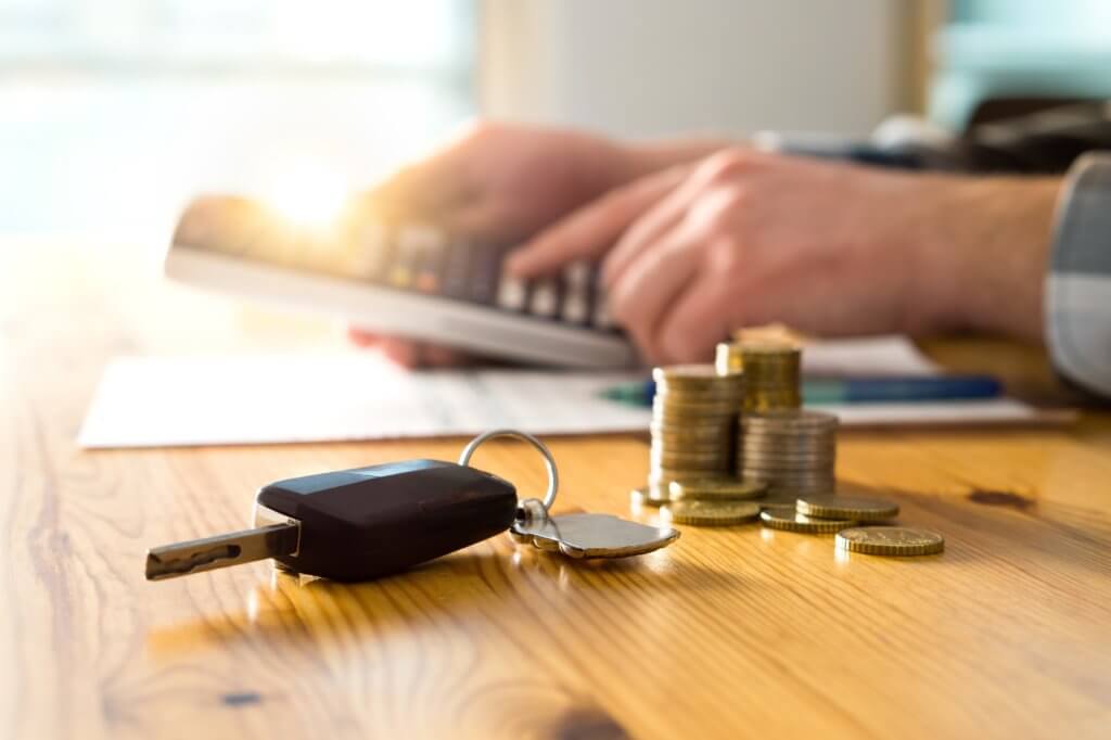 A man using a calculator, with car keys and coins in the foreground