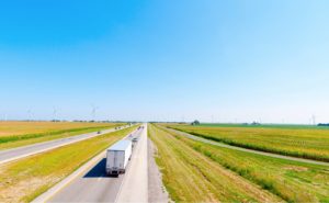 A truck driving down a road with green fields on either side and wind turbines in the background