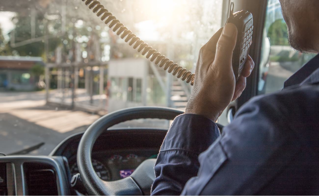 The inside of a truck cockpit, with the driver speaking into a radio handset.