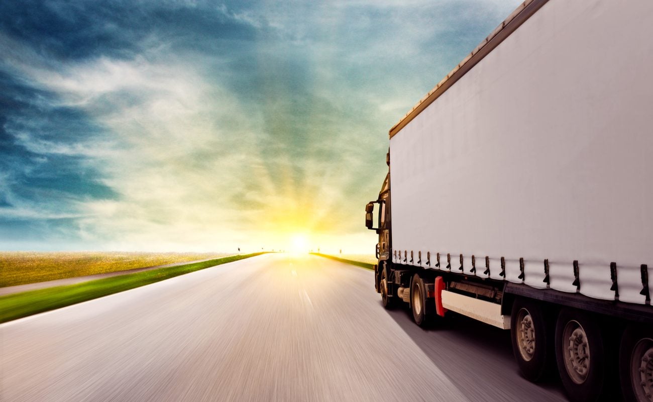 A tractor and trailer truck driving into the sunset